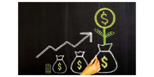 Chalkboard illustration of financial growth: three increasing money bags with dollar signs, rising arrow, coins, and a money tree being drawn by hand.